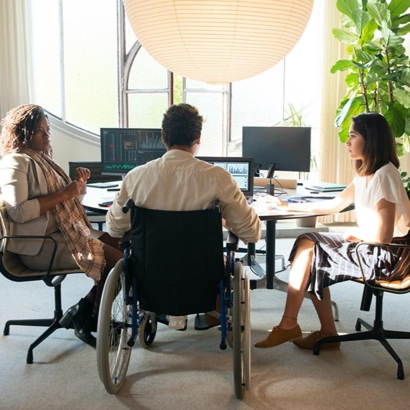Three people sat around a meeting table. One person is in a wheelchair.