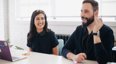 Young woman smiling sat at a desk with a man