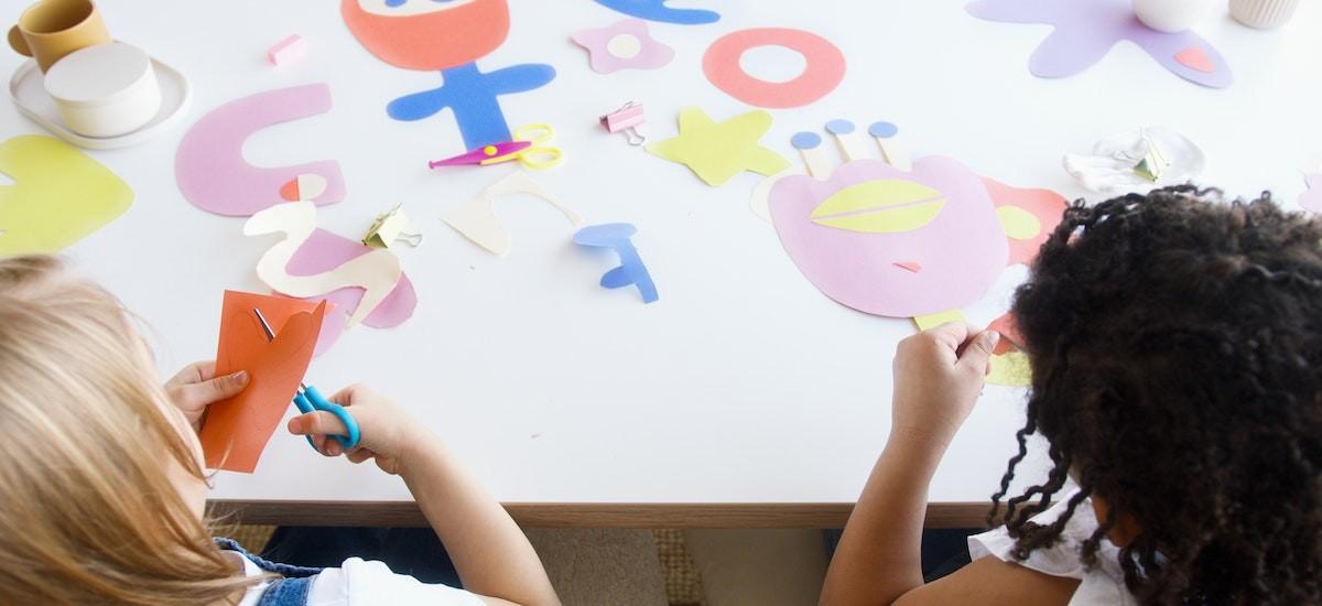 Two children cutting coloured paper with scissors