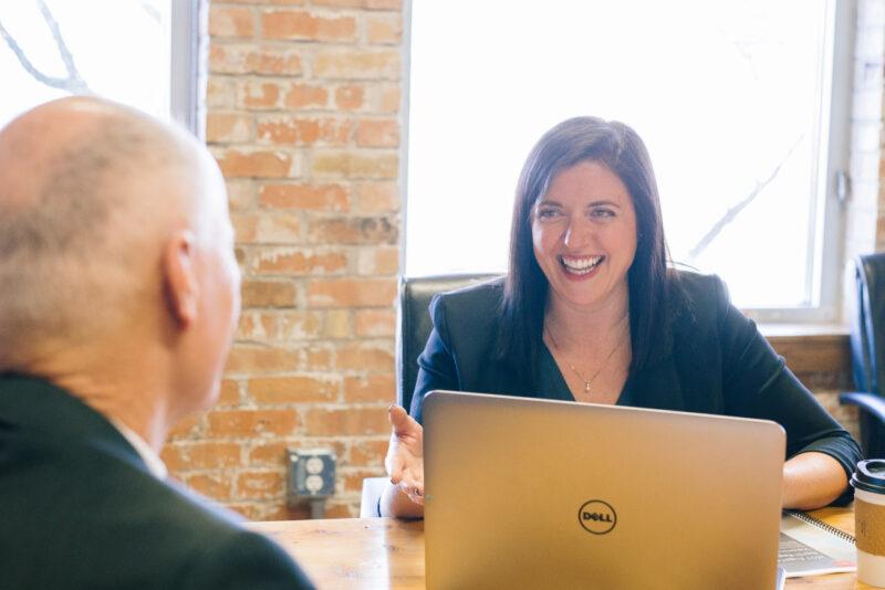 Man and women sat across a meeting table with a laptop